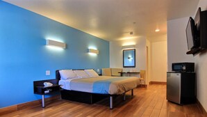 A modern hotel room with a bed, bedside table, and a small refrigerator.