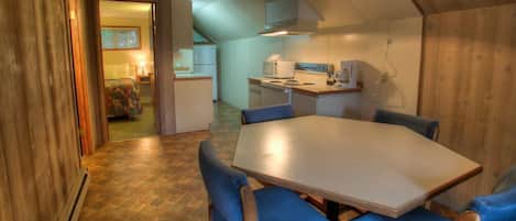 A cozy room with a wooden interior, a dining table with chairs, a kitchenette, and a bed with a colorful blanket.