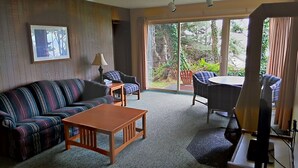 A living room with a striped sofa, a wooden coffee table, a lamp, and a view of the outdoors through large windows. - Ocean Crest Resort (Moclips)