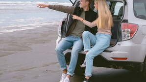 A couple sitting in the back of a vehicle with the trunk open, overlooking a beach. - Ocean Crest Resort (Moclips)