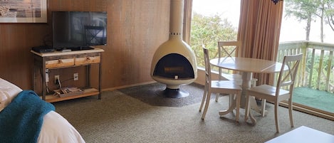 A hotel room with a bed, a television, a fireplace, a dining table with chairs, and a balcony with curtains.