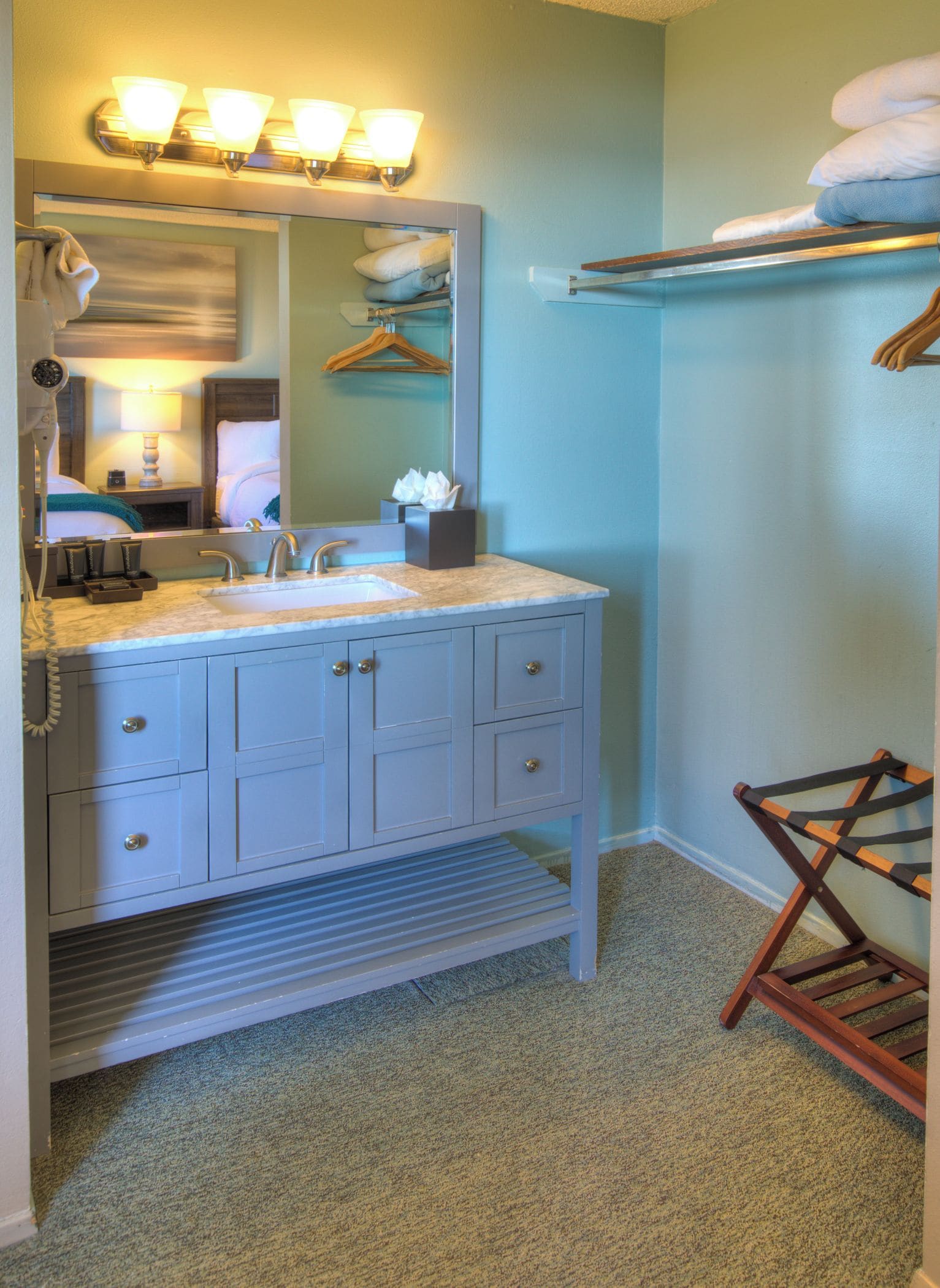 A bathroom with a vanity, sink, mirror, towel rack, and a hanging towel rack.