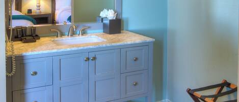 A bathroom with a vanity, sink, mirror, towel rack, and a hanging towel rack.