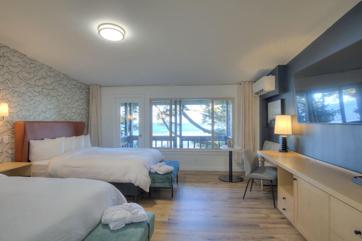A hotel room with two beds, a desk, and a view of the ocean.