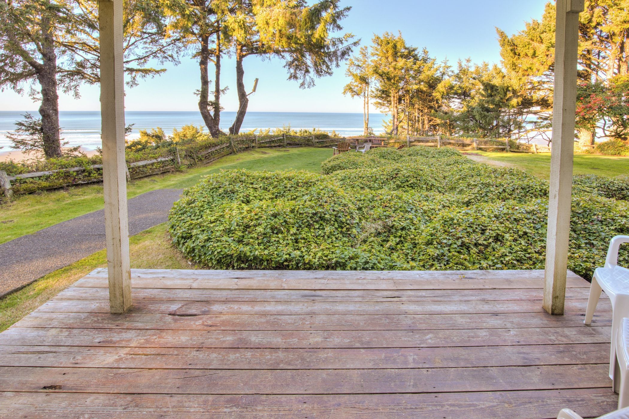 A wooden deck with a view of a landscaped garden and the sea.
