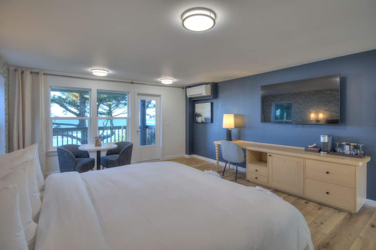 A hotel room with a large bed, a desk with a lamp, a TV, and a view of the outdoors.