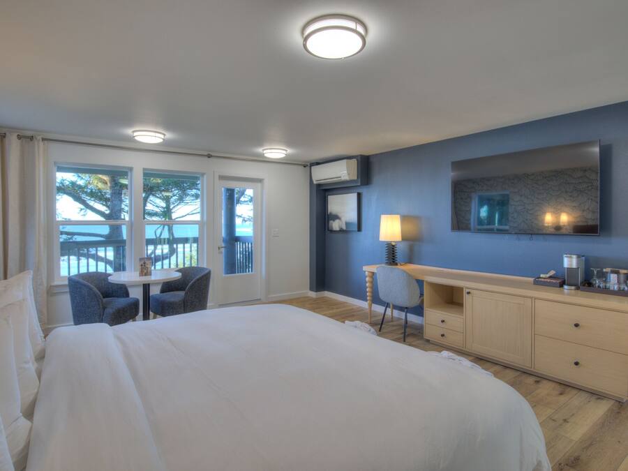 A hotel room with a large bed, a desk with a lamp, a TV, and a view of the outdoors.