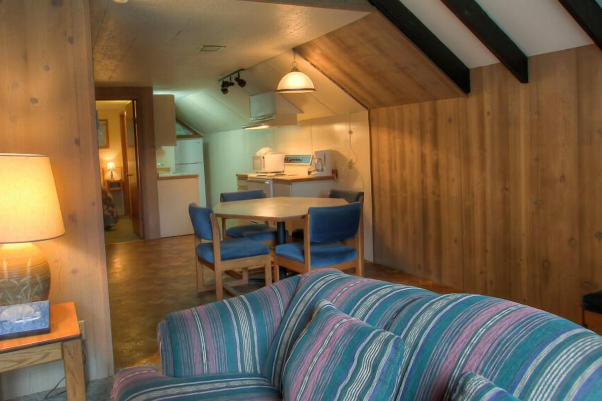 A cozy room with a striped sofa, a small table with a lamp, and a dining area with a table and chairs.
