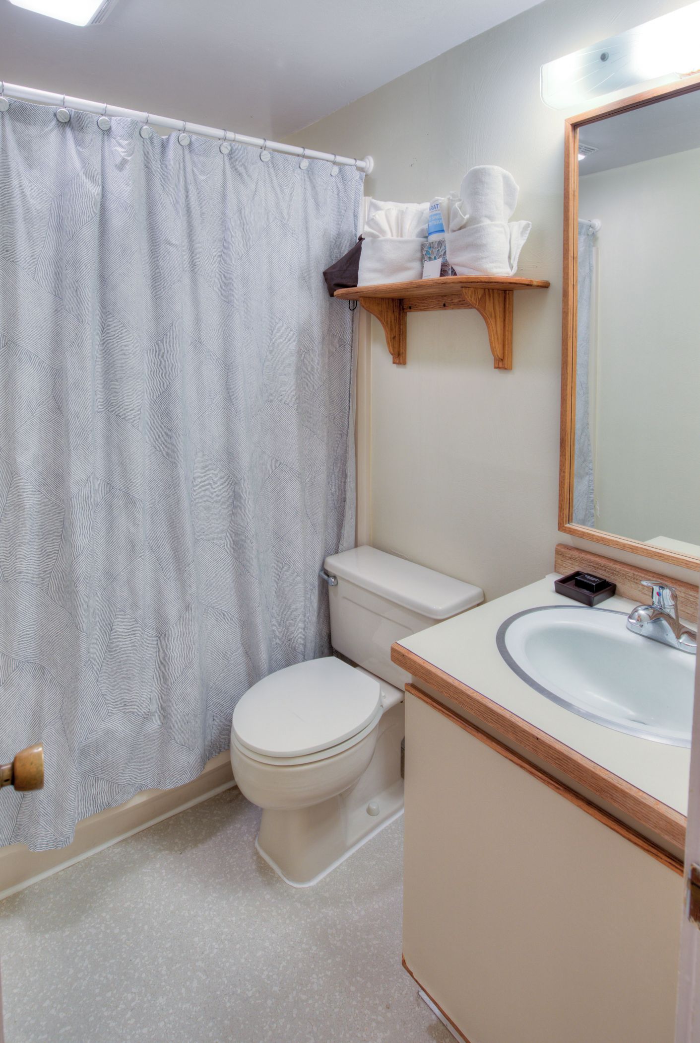 Une salle de bain comprenant des toilettes, un lavabo, un miroir, un rideau de douche et une étagère avec des articles de toilette.