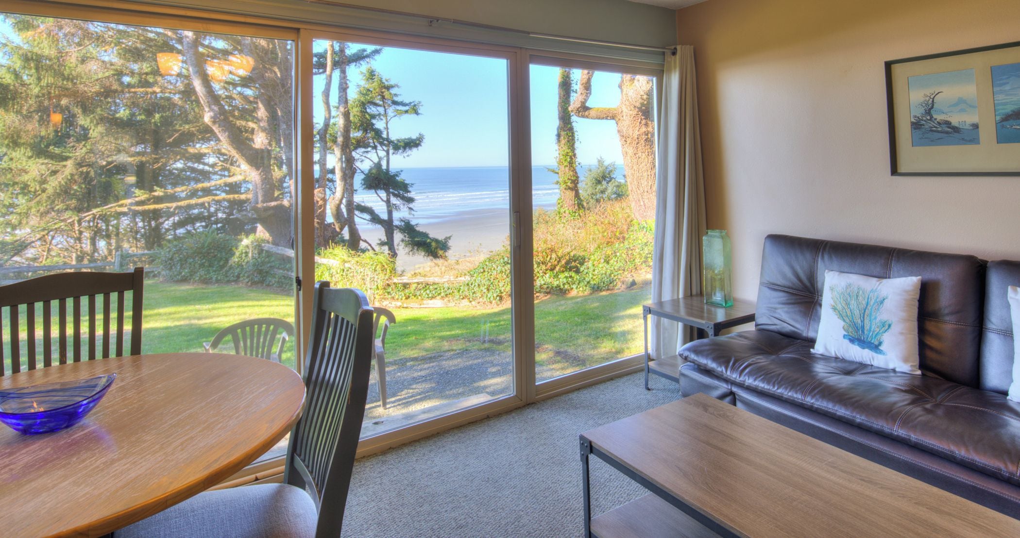 A room with a view of the beach, a dining table, a sofa, and a chair.