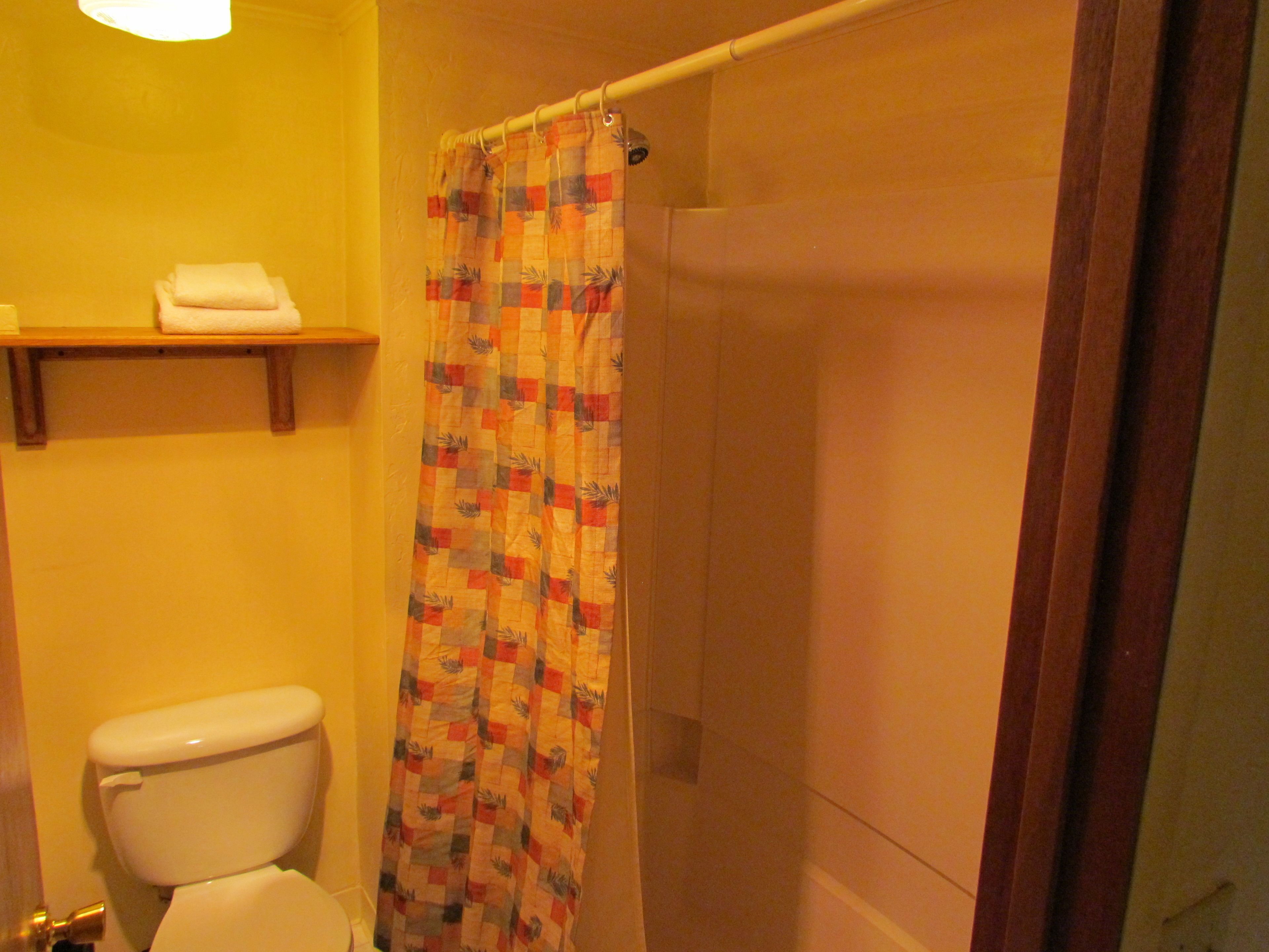 A bathroom with a toilet, a shower curtain, and a shelf with a towel.