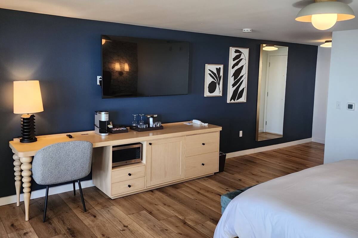 A hotel room with a bed, a desk with a lamp, a microwave, and a large mirror.