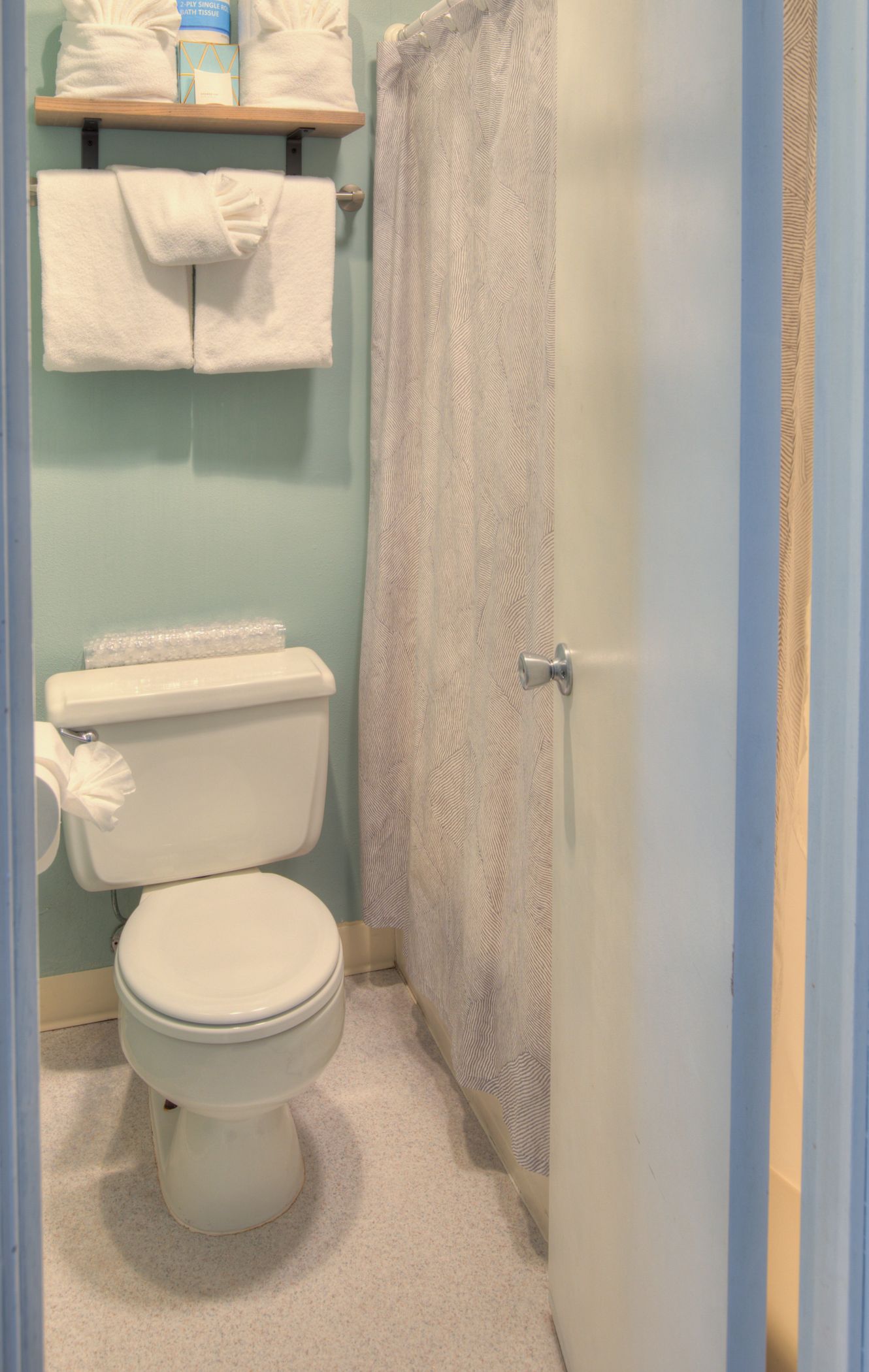 A bathroom with a toilet, a shower curtain, and a shelf with towels.