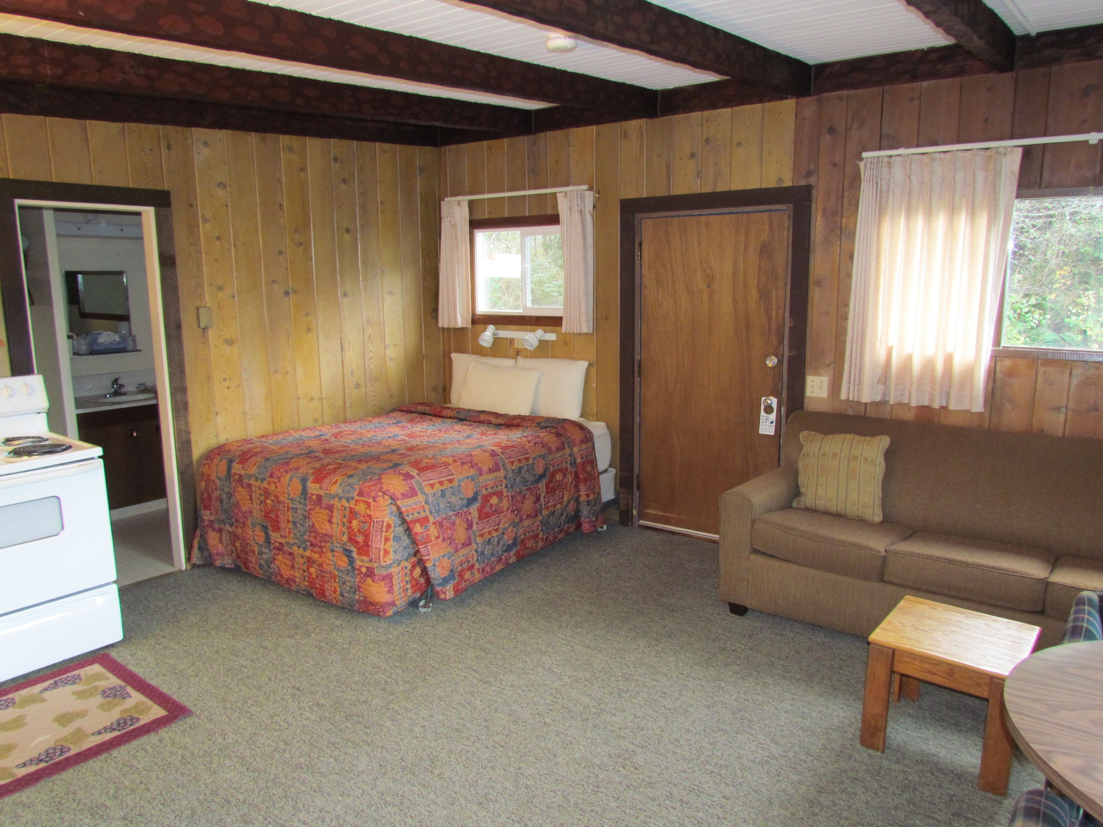 Una habitación con cama, sofá, una mesita, cómoda y ventana con cortinas.