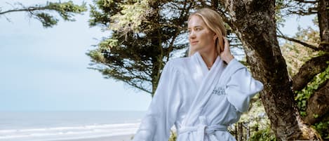 A person in a white robe standing by a wooden railing overlooking a beach.
