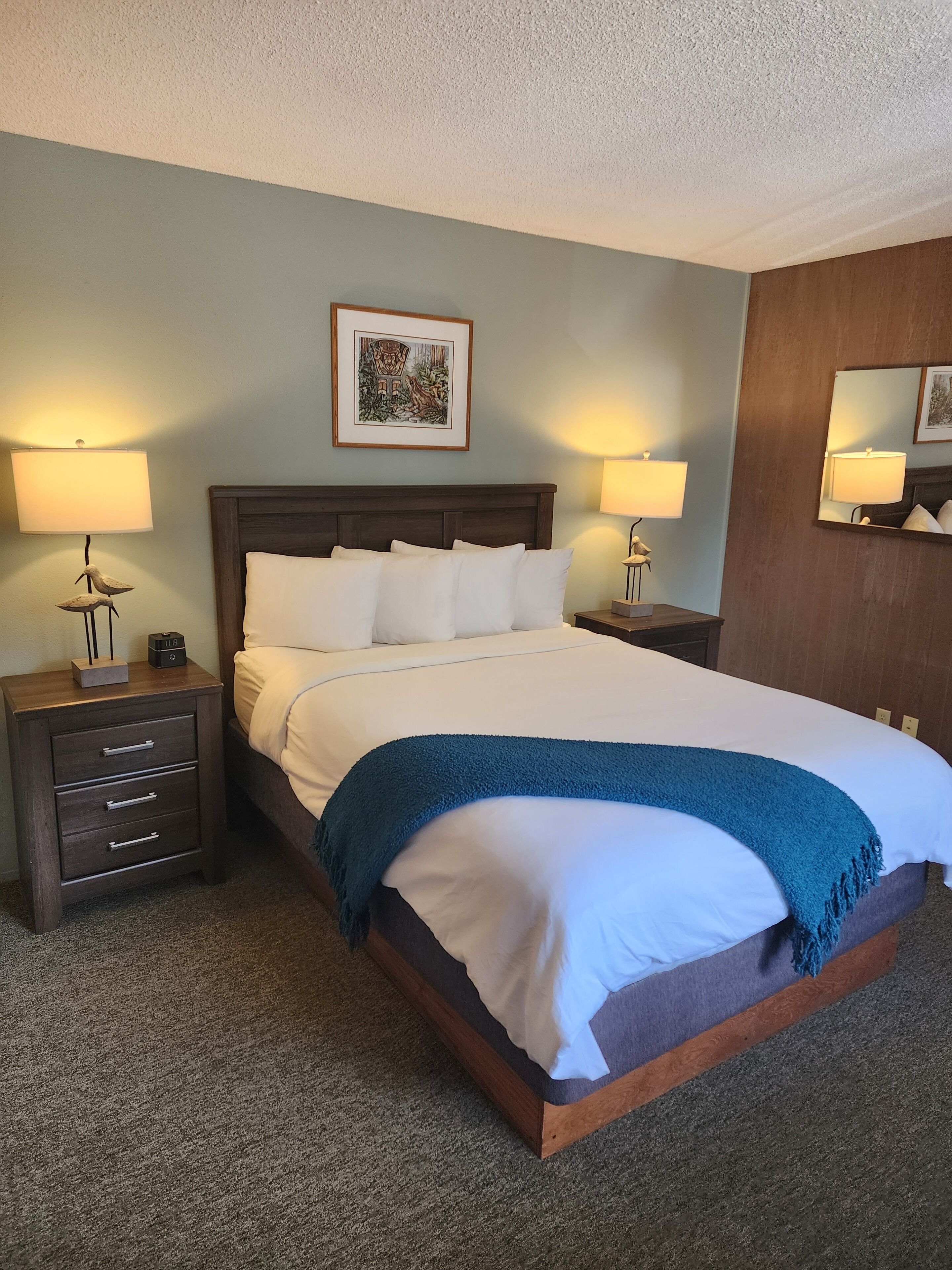 A neatly made bed with white linens and a blue throw blanket, flanked by two bedside tables with lamps and a small decorative item.