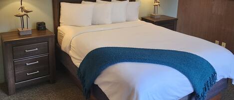 A neatly made bed with white linens and a blue throw blanket, flanked by two bedside tables with lamps and a small decorative item.
