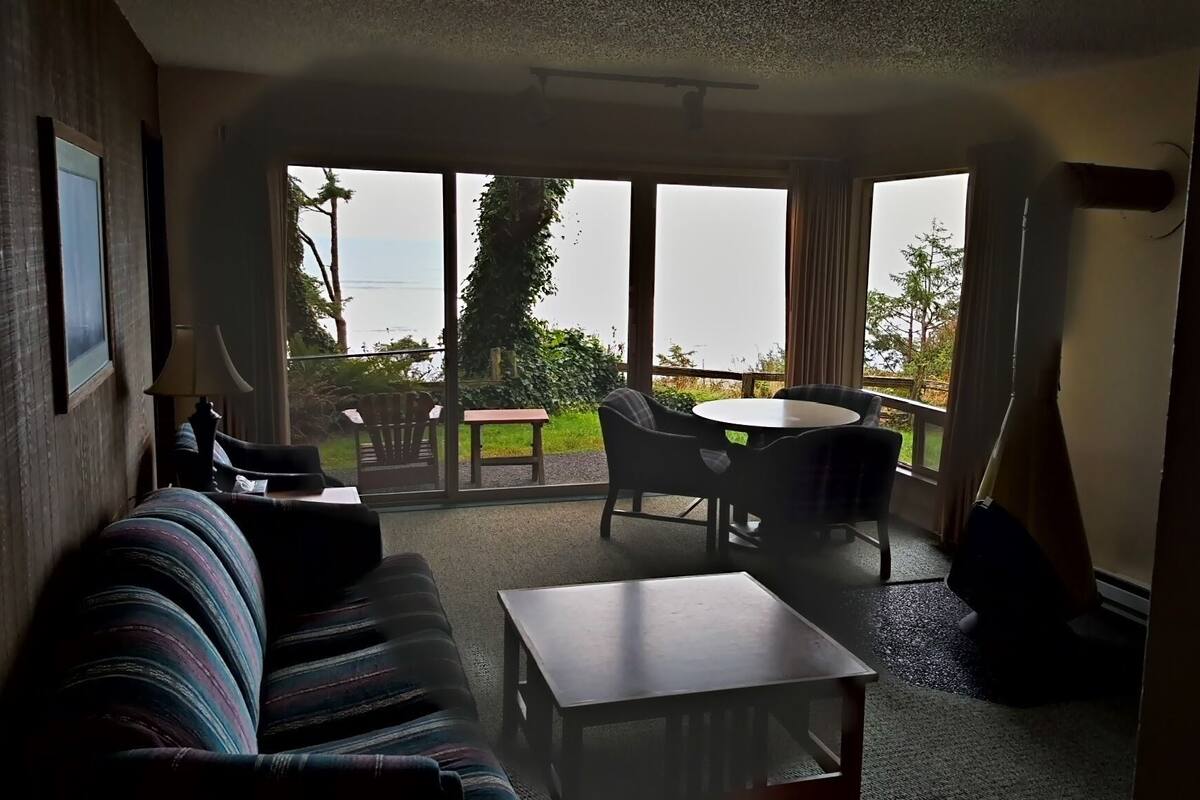 A living room with a sofa, a small table, and a view of the outdoors through large windows.