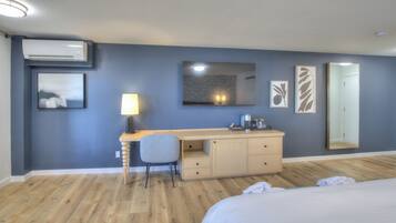 A hotel room with a bed, a desk with a chair, a wardrobe, a mirror, and artwork on the walls.
