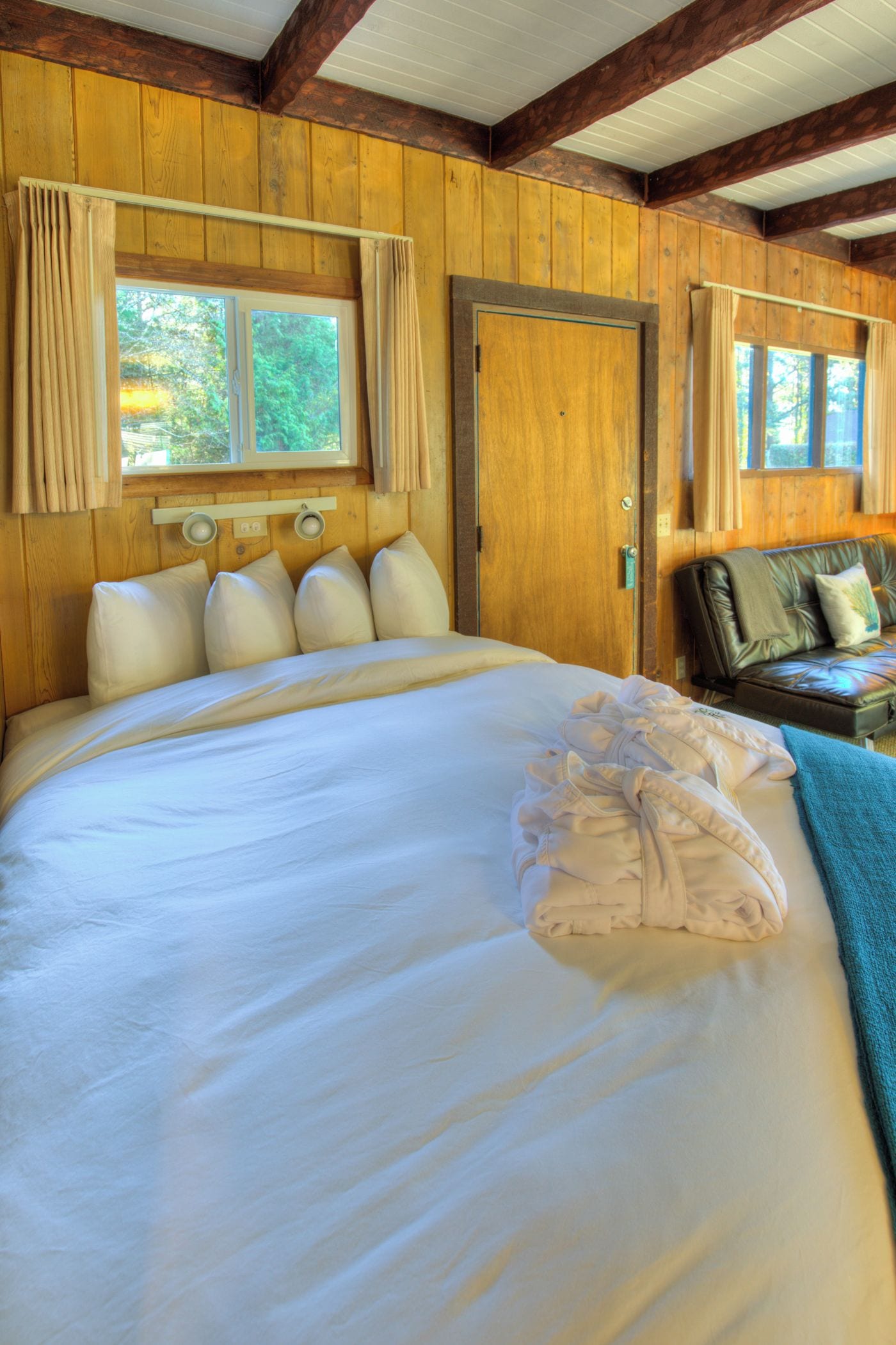 A large bed with a headboard, a wooden wall, a window with curtains, and a door.