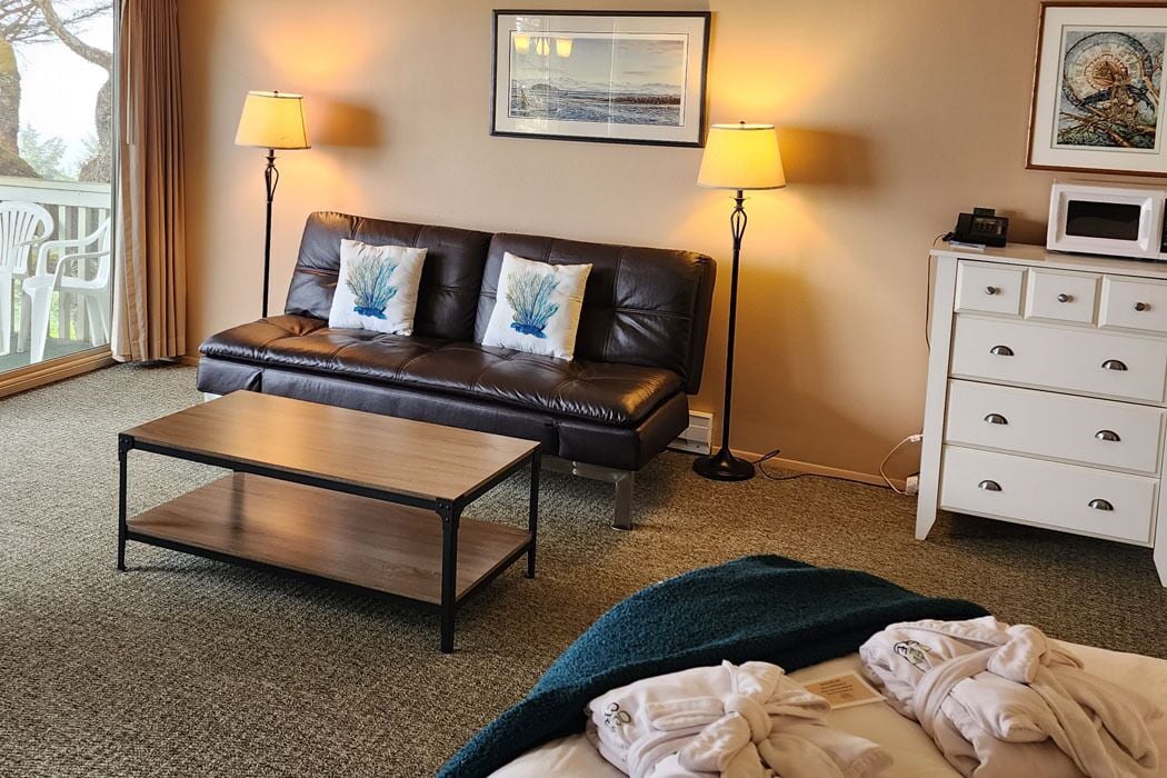 A hotel room with a leather sofa, a wooden coffee table, a white dresser, and two lamps.