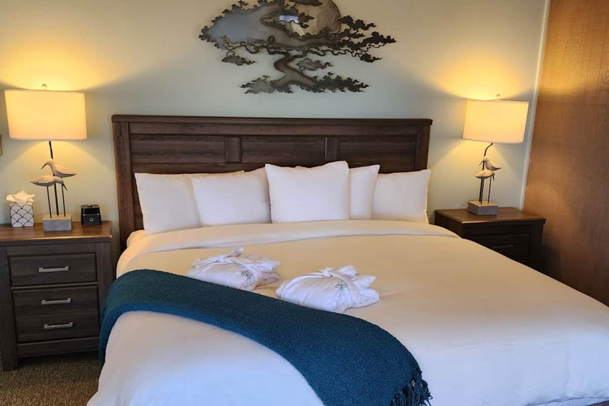 A neatly made bed with white linens and a teal throw blanket, flanked by two bedside tables with lamps and decorative items.
