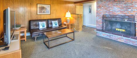 Una sala de estar con un sofá de cuero, una mesa de centro, una chimenea y un televisor.