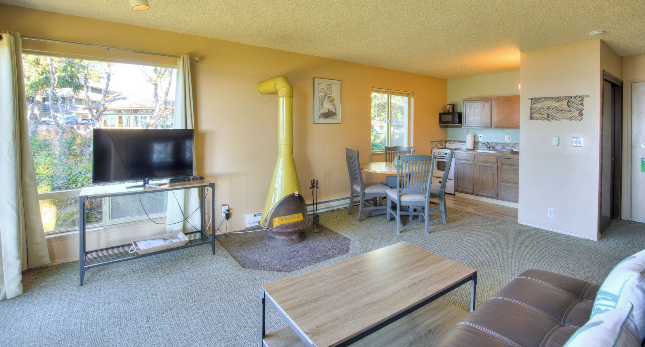 A living room with a television, a yellow chimney, a dining table with chairs, and a kitchen area.