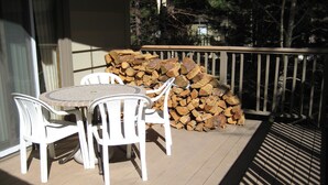 A patio with a table and chairs, a stack of firewood, and a railing. - Chateau Sans Nom by Mammoth Reservation Bureau (Mammoth Lakes)