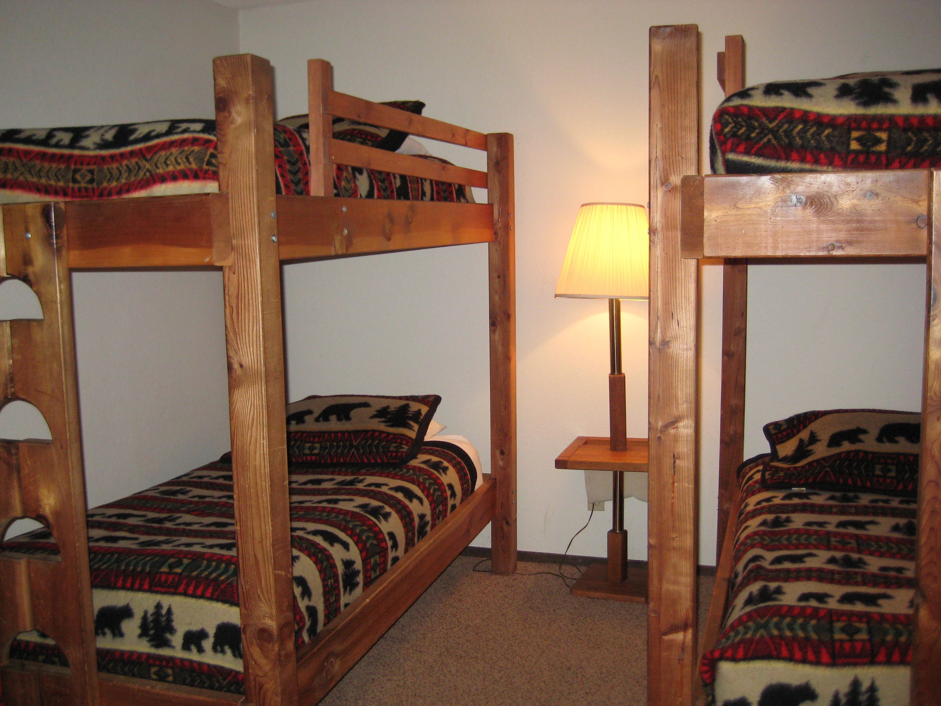 A bunk bed room with a wooden frame, a bedside table with a lamp, and patterned bedding.