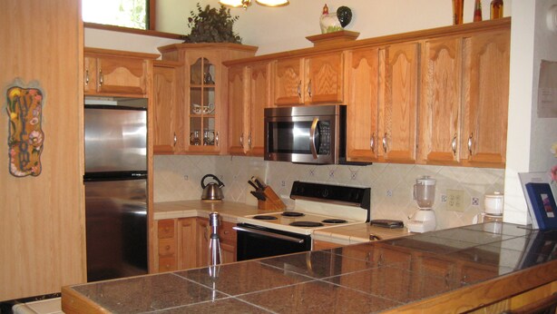 A kitchen with wooden cabinets, a stainless steel refrigerator, a microwave, an oven, and a granite countertop. - Chateau Sans Nom by Mammoth Reservation Bureau (Mammoth Lakes)