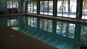 An indoor swimming pool with clear glass walls, wooden beams on the ceiling, and a view of the outside. - Chateau Sans Nom by Mammoth Reservation Bureau (Mammoth Lakes)