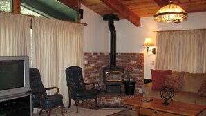 A cozy living room with a brick fireplace, leather chairs, a television, and a wooden coffee table. - Chateau Sans Nom by Mammoth Reservation Bureau (Mammoth Lakes)