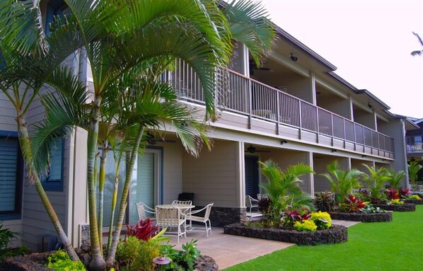 Un bâtiment à deux étages doté d’un balcon, d’un espace extérieur aménagé pour s’asseoir et d’un jardin paysager aux allures tropicales.