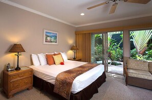 Une chambre d’hôtel avec un lit, deux tables de chevet, une petite table, une chaise et une vue sur la verdure à travers la porte vitrée.