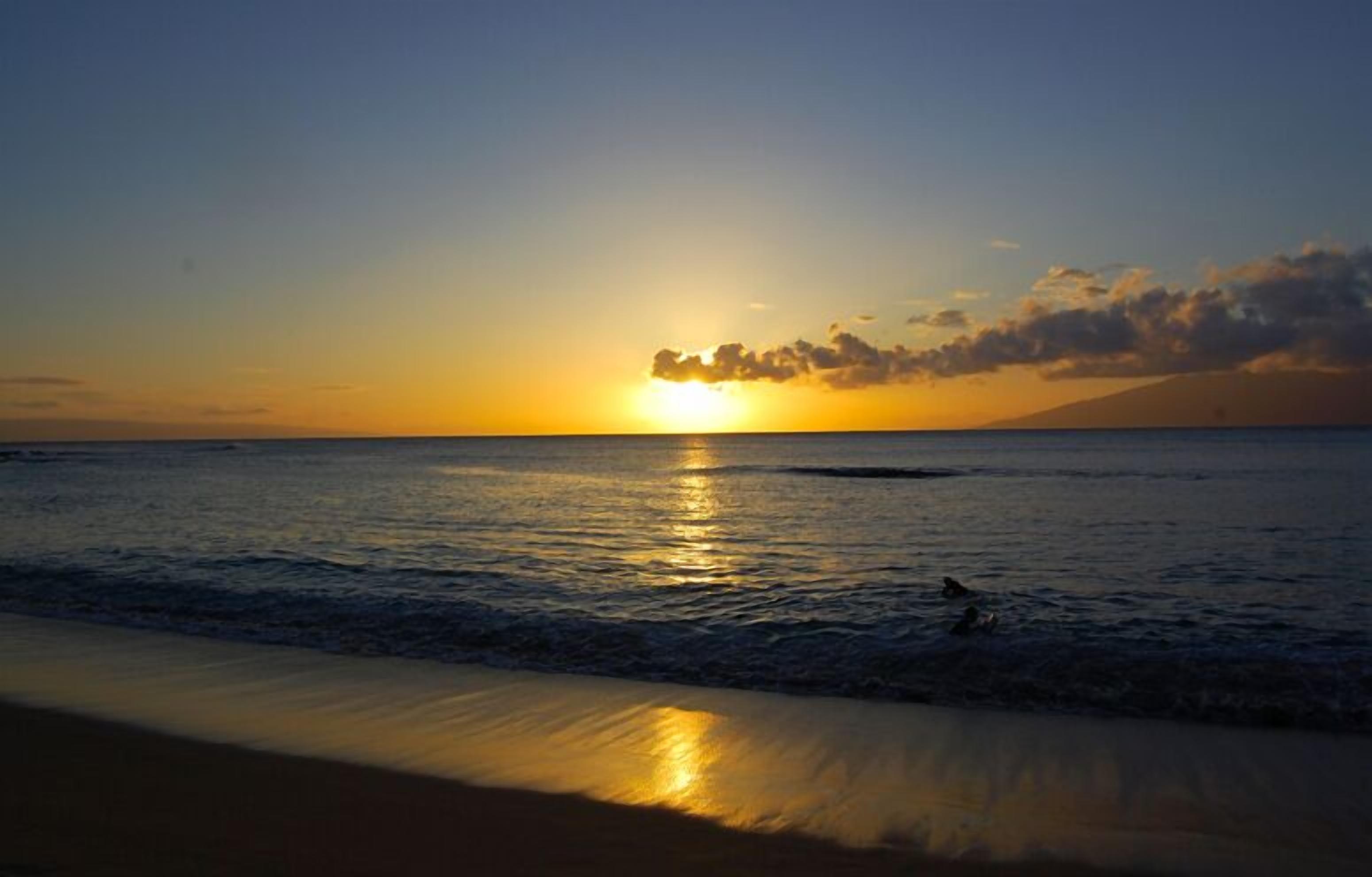Een zonsondergang boven een strand met rustige golven en een heldere lucht.