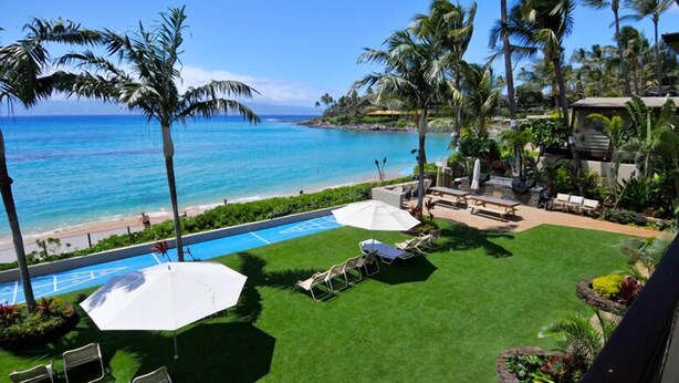 A pool area with a view of the ocean, surrounded by palm trees and lounge chairs. - Hale Napili (Lahaina)