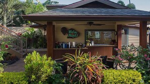 A small, cozy building with a sign reading "Hale Napili." It features a covered porch with a ceiling fan, surrounded by lush greenery and various plants. - Hale Napili (Lahaina)