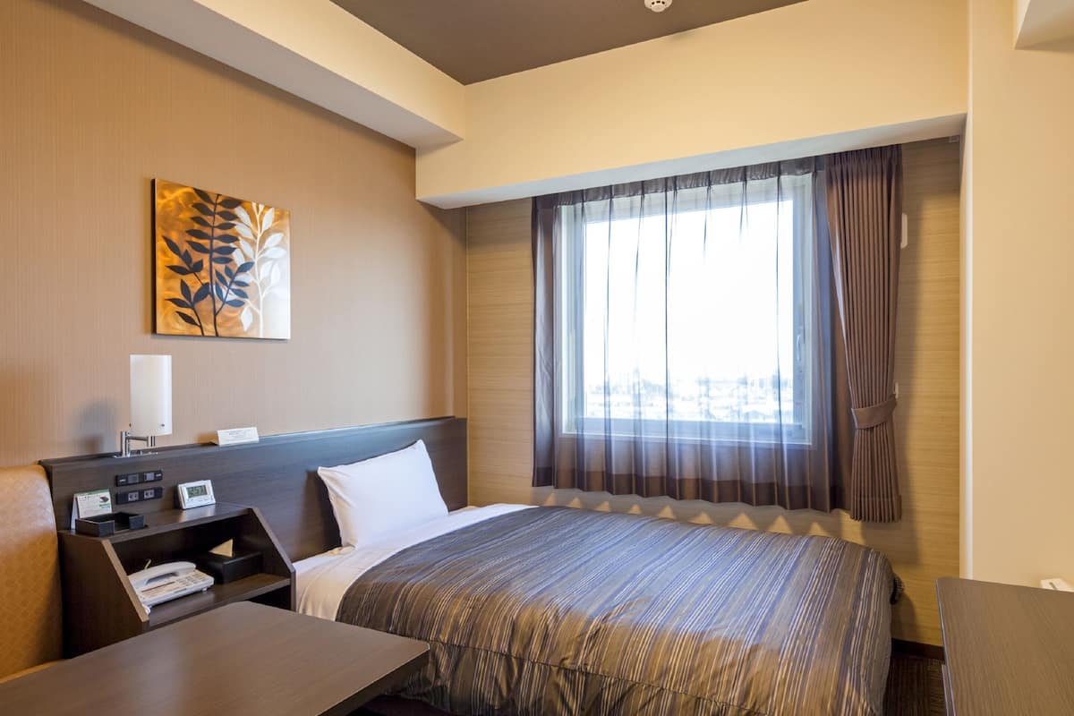 A hotel room with a bed, a desk, a telephone, and a window with curtains.