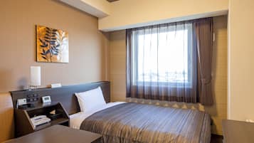 A hotel room with a bed, a desk, a telephone, and a window with curtains.