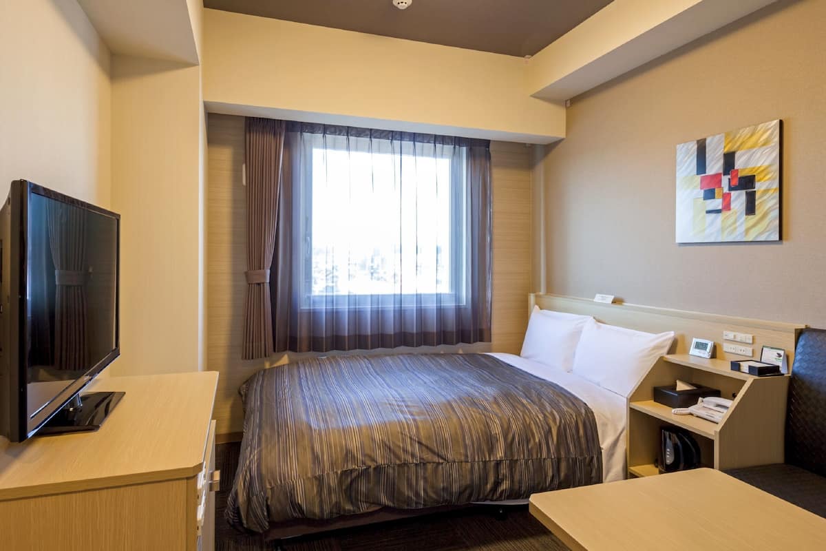 A hotel room with a bed, a desk, a television, and a painting on the wall.