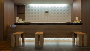 A reception area with a wooden reception desk, two wooden stools, a patterned wall, and a ceiling light fixture. - Hotel Route Inn Minami Yokkaichi (Yokkaichi)