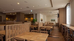 A restaurant with wooden furniture, a plant, and a painting on the wall. - Hotel Route Inn Minami Yokkaichi (Yokkaichi)