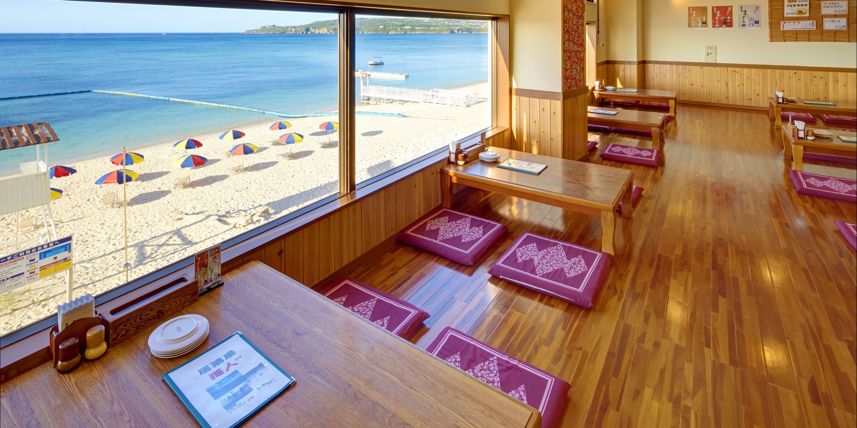 A restaurant with wooden furniture and large windows overlooking a beach.
