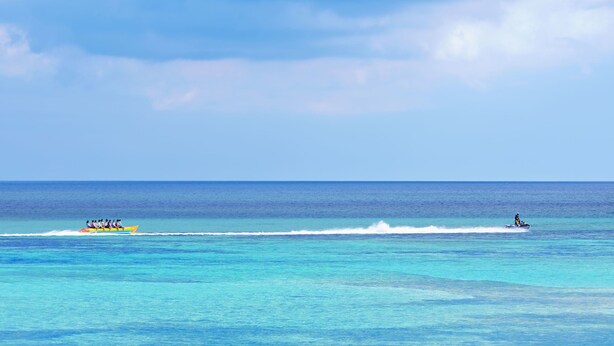 Una vista despejada del océano con un bote amarillo y un jet ski a lo lejos.