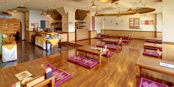 Interior de restaurante com mesas de madeira, almofadas roxas e luminárias pendentes.