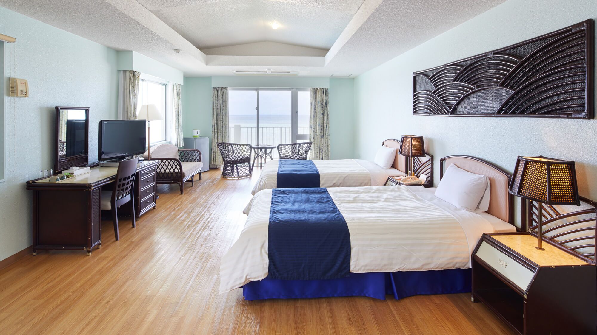 Habitació d'hotel amb dos llits, un escriptori, una televisió i vista al mar.