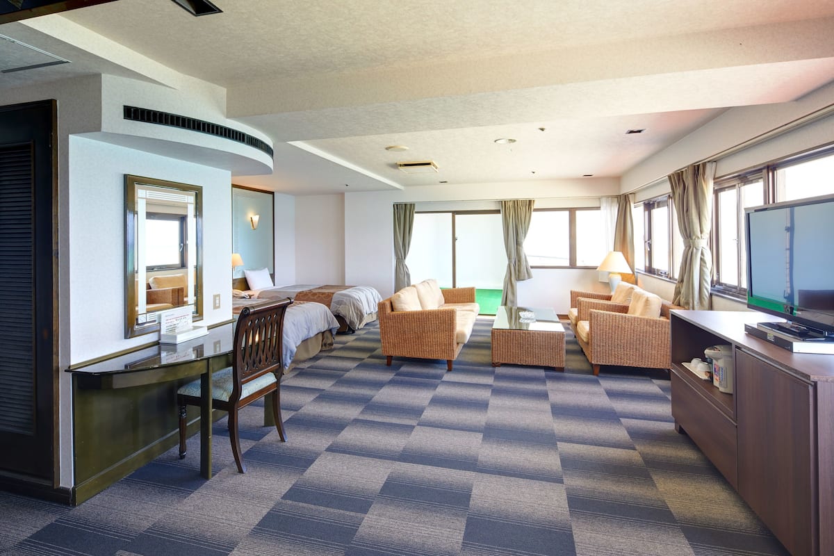 Ett hotellrum med en säng, två soffor, en tv, ett skrivbord och ett fönster med gardiner.