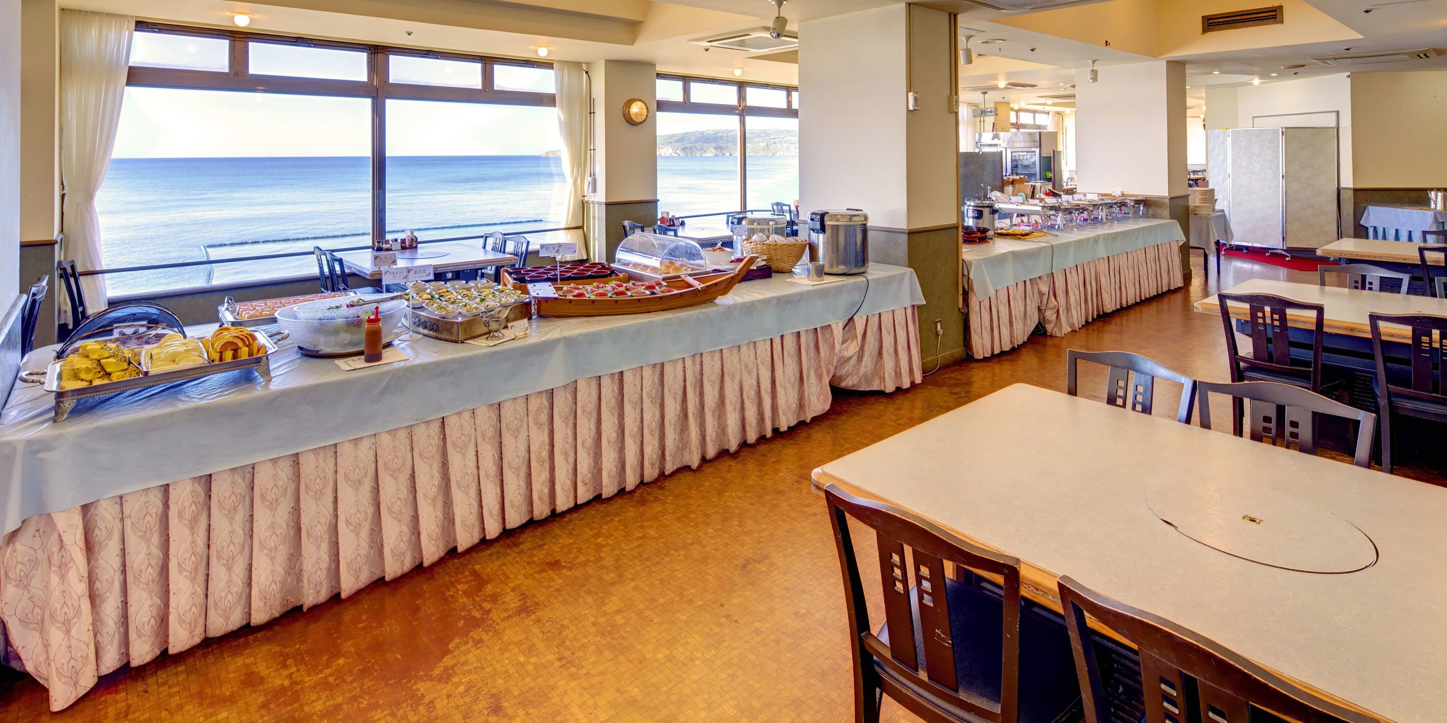 A buffet setup with a view of the ocean, featuring various food items and a long table with a tablecloth.
