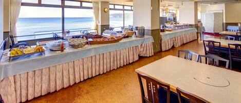 A buffet setup with a view of the ocean, featuring various food items and a long table with a tablecloth.